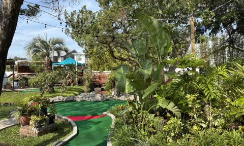 A long hole on a miniature golf course with green foliage along on side