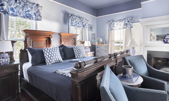 This large guest room features a blue and white decor, an imposing wooded bed, and a pair of comfortable chairs