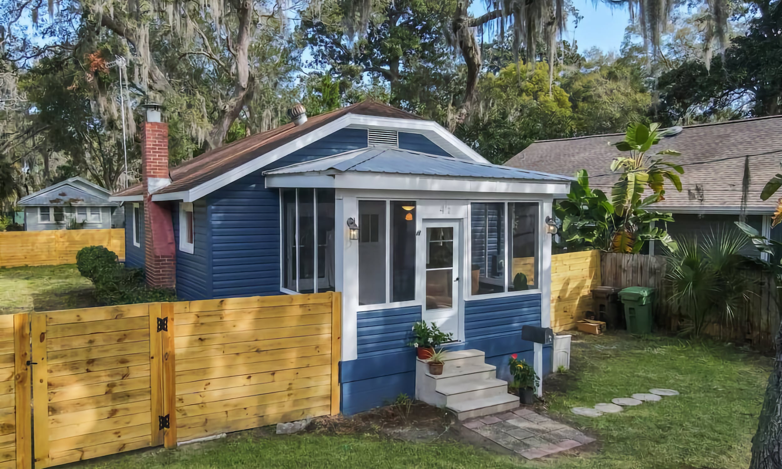 A blue and white historic bungalow with a fenced-in backyard