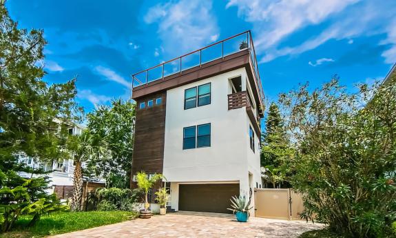 The three-story vacation rental has a brick driveway and a fence to the yard