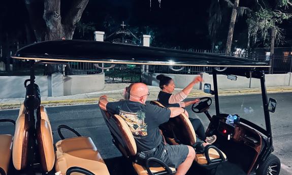 Guests in a golf cart, learn about Tolomato Cemetery from their tour guide