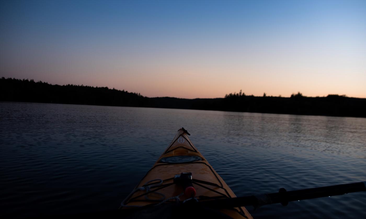 A beautiful sunset hovers over tranquil waters and a small yellow kayak.