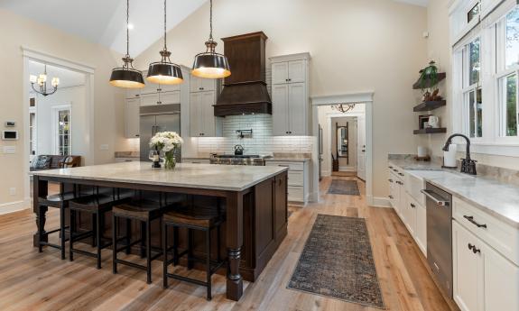 The kitchen has white cabinets, a dark wood island with stools on two sides, and a gas stove
