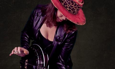 Mean Mary wears a black jacket and poses in front of a black backdrop.