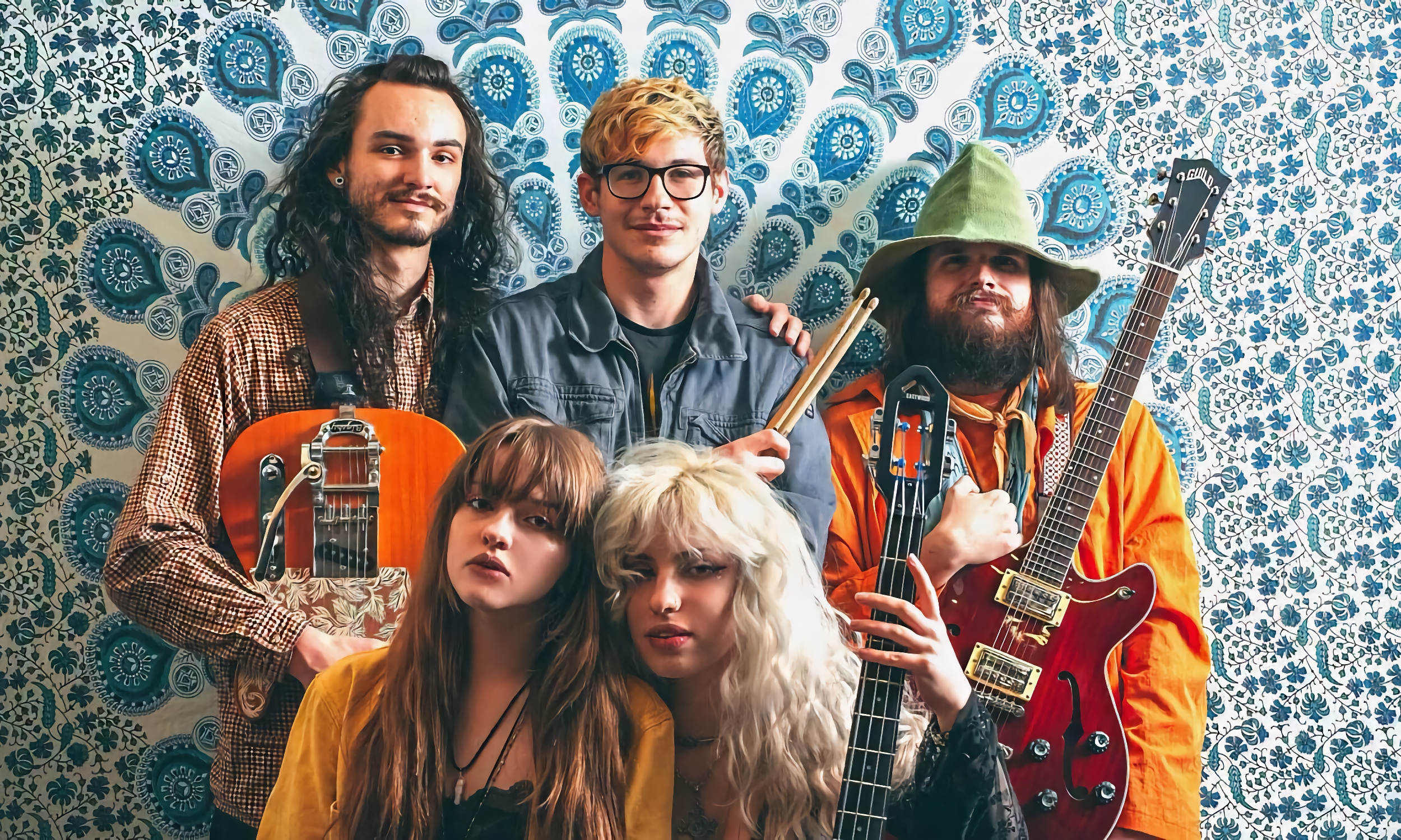 Five band members, wearing colorful clothing, in front of a tiled wall in teal