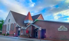 A brick church building during the day, with several different roof lines including a spire in the center