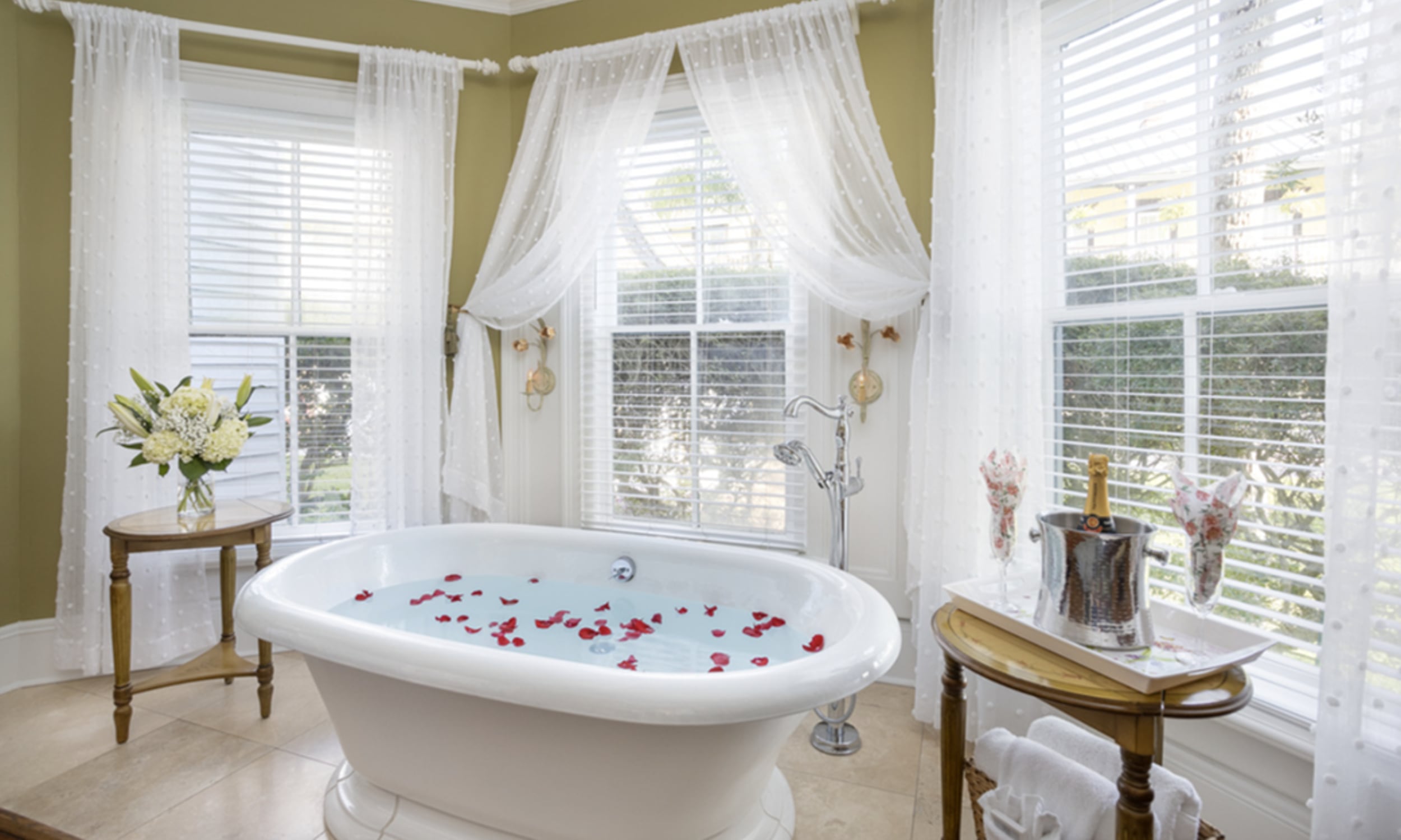 Bathtub filled with rose petals in front of three panoramic windows at Bayfront Westcott Inn