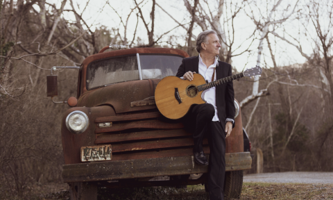 Ellis Paul clutches his guitar while leaning on a classic car.