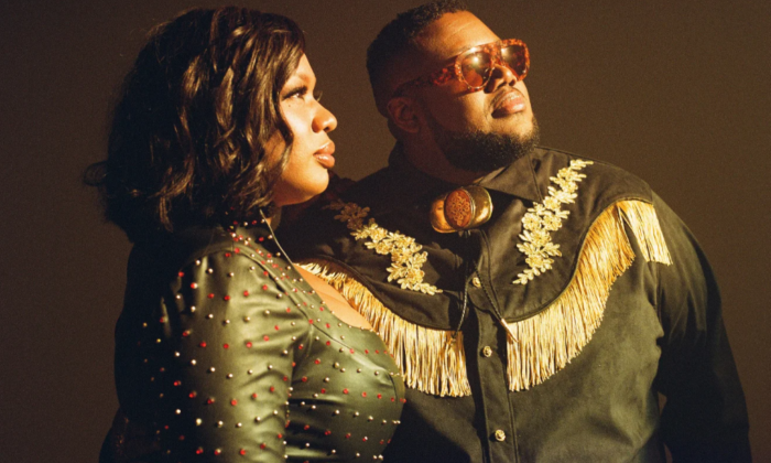 Bandmates from The War and Treaty wear black clothing and pose in front of a dark brown backdrop.